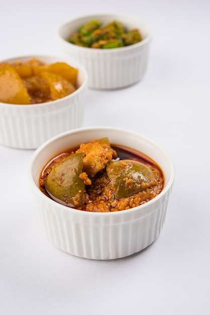 Group photograph of indian pickles like mango pickle , lemon pickle and green chilli pickle, sarved in black ceramic bowl, selective focus