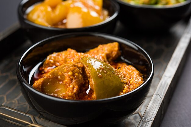 Group photograph of indian pickles like mango pickle , lemon pickle and green chilli pickle, sarved in black ceramic bowl, selective focus