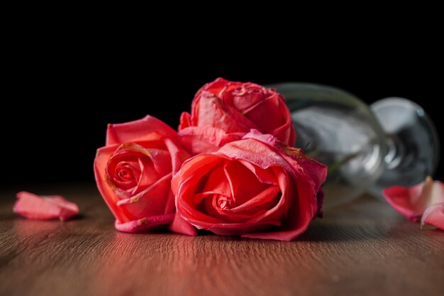 Un gruppo di rose rosa mette in un bicchiere di champagne che cade sul tavolo di legno di colore scuro