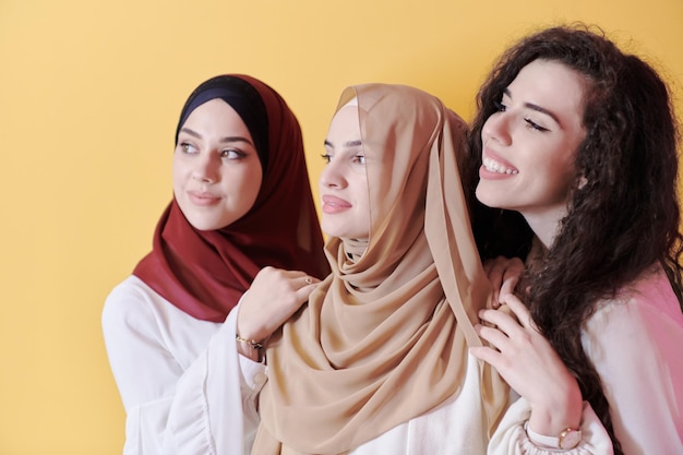 group portrait of beautiful muslim women two of them in fashionable dress with hijab isolated on yellow background representing modern islam fashion and ramadan kareem concept