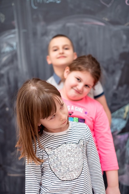 검은 칠판 앞에서 즐거운 시간을 보내면서 서로 뒤에 서 있는 행복한 아이들의 그룹 초상화