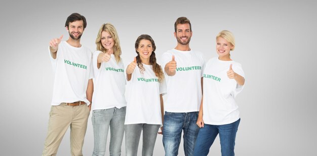 Group portrait of happy volunteers gesturing thumbs up against grey vignette