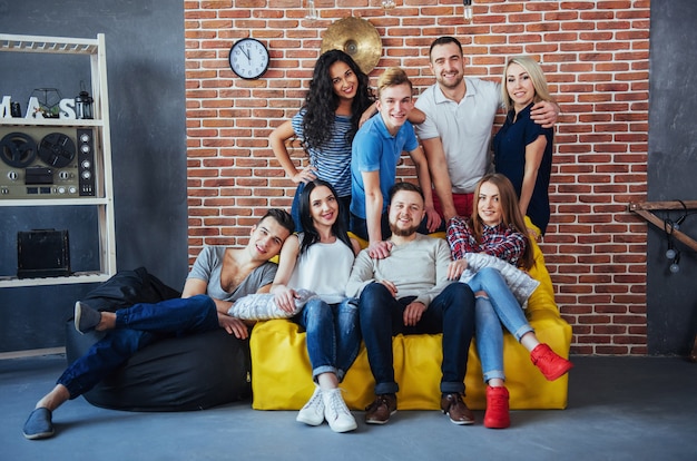 Group portrait of multi-ethnic boys and girls with colorful fashionable clothes holding friend posing on a brick wall, Urban style people having fun, s about youth togetherness lifestyle