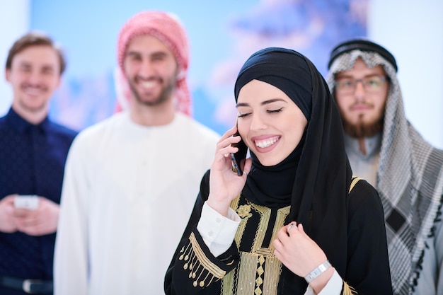 Foto ritratto di gruppo di giovani musulmani donna in abito hijab alla moda con tre uomini arabi che utilizzano smartphone in una moderna casa luminosa che rappresenta la moderna tecnologia della moda islamica e il ramadan kareem con