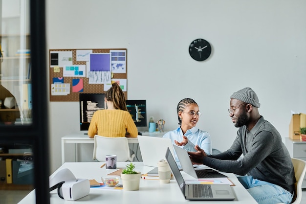 group of programmers discussing computer program in office while sitting at table with computers