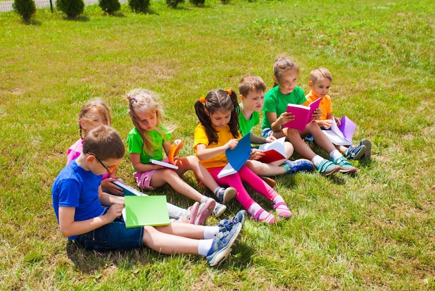 Group of pupils in colorful clothes sit on the lawn and read books outdoors