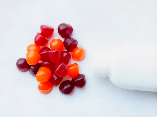 Group of red, orange and purple multivitamin gummies with the bottle isolated on white background. Healthy lifestyle concept.