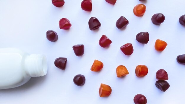 Group of red, orange and purple multivitamin gummies with the bottle isolated on white background. Healthy lifestyle concept.