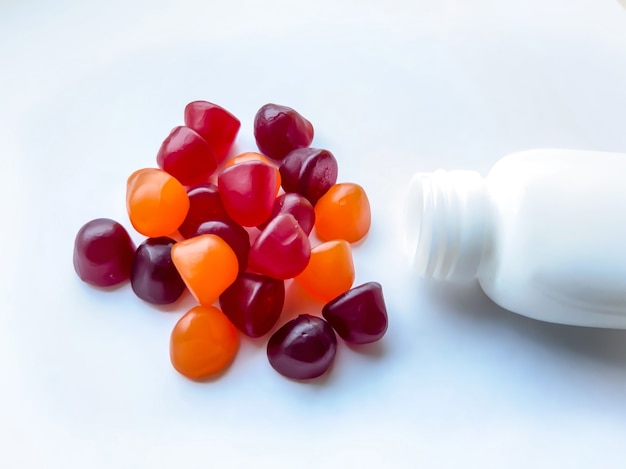 白の背景に分離されたボトルと赤、オレンジ、紫のマルチビタミングミのグループ。健康的なライフスタイルのコンセプト。