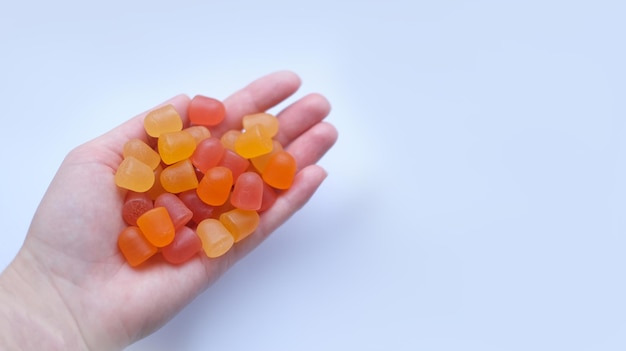 Group of red orange and yellow multivitamin gummies in the hand isolated on white background