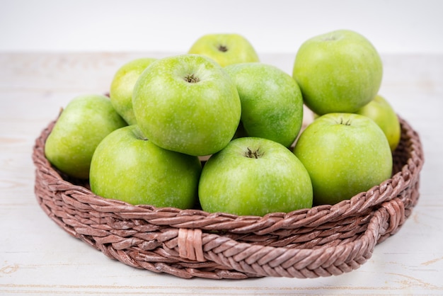 Group of ripe green apples in a basket on white surface