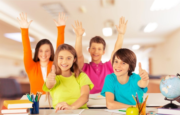 Group of school kids in classroom with hands raised