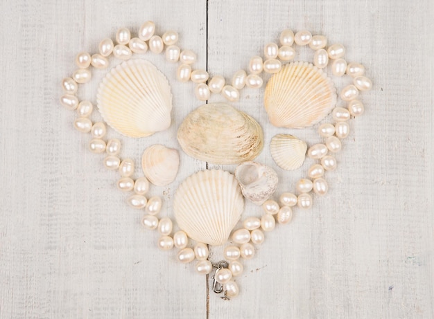 Photo the group of sea shells and pearls laid out in the shape of heart on white wooden background