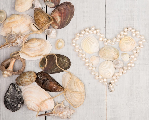 Foto il gruppo di conchiglie e perle disposte a forma di cuore su fondo di legno bianco