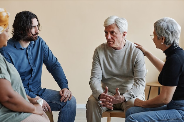 Group of senior people sitting in circle at mental health support group with white haired man sharin