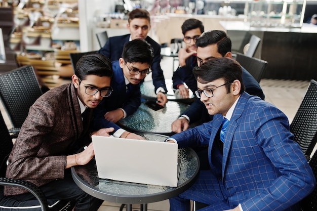 Group of six indian business man in suits sitting at office on cafe and looking at laptop