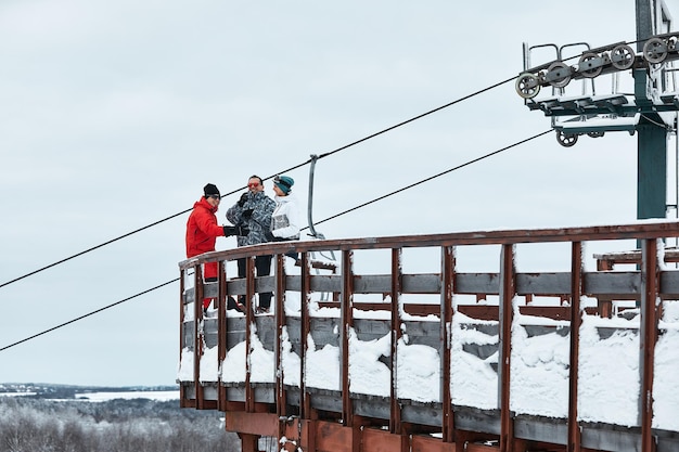 Group of skiers friends on the mountain are resting and drinking coffee from a thermos on the background of the ski lift.