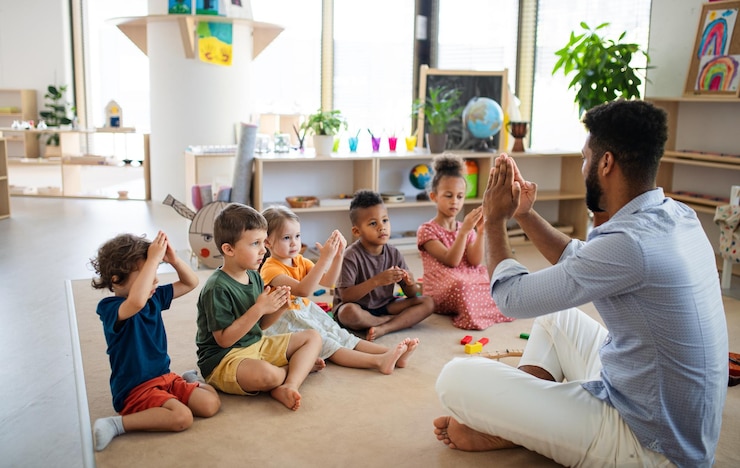 Photo group of small nursery school children with man teacher sitting on floor indoors in classroom playing