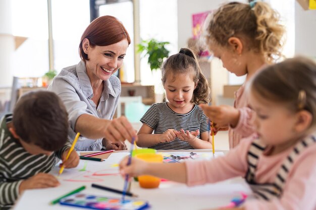 group of small nursery school children with teacher indoors in classroom painting
