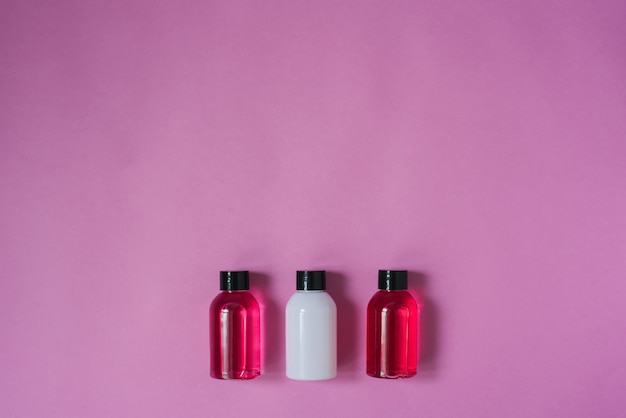 Group of small travel bottles for body care: shower gel, shampoo, balm, lotion on pink background. The composition of the flat layer of cosmetics Copy space.