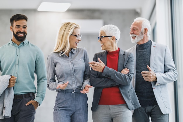 A group of a smiling business people walking through the modern office and having a discussion with each other during the meeting.