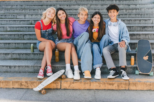 Group of smiling friends stylish multiracial teenagers sitting on stairs with skateboards friendship