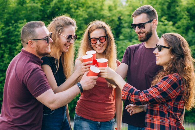 Группа улыбающихся друзей поджаривания безалкогольных напитков в красной картонной чашке