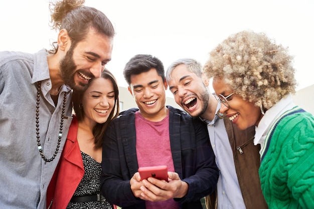 Группа улыбающихся друзей вместе с помощью телефонов счастливые люди смотрят что-то на мобильном телефоне