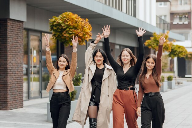 Group of smiling and happy teenage friends wearing casual clothes spending time together posing and talking with each other near college building on autumn day