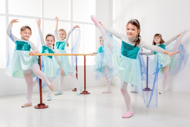 Group of a smiling little girls using barre while practicing in dance studio.