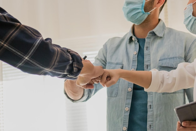 Group of smiling young caucasian, asian colleagues or contractors, engineer wearing face masks and bumping elbows to protection at workplace while coronavirus is pandemic.Greeting in Covid concept,