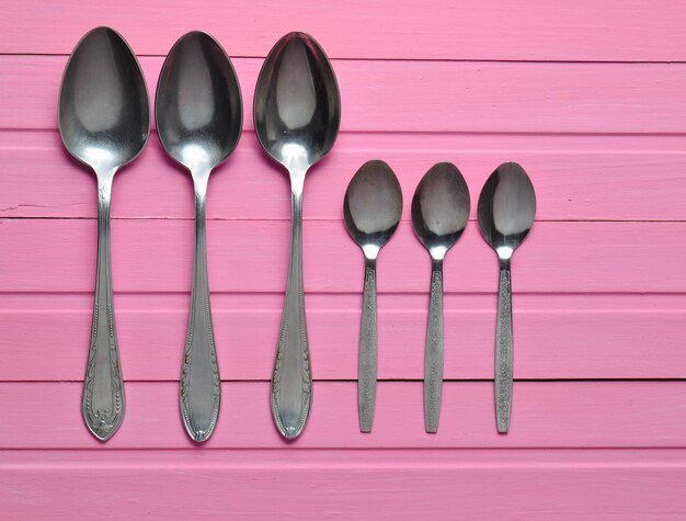 A group of spoons on a pink wooden table. Cutlery. Top view.