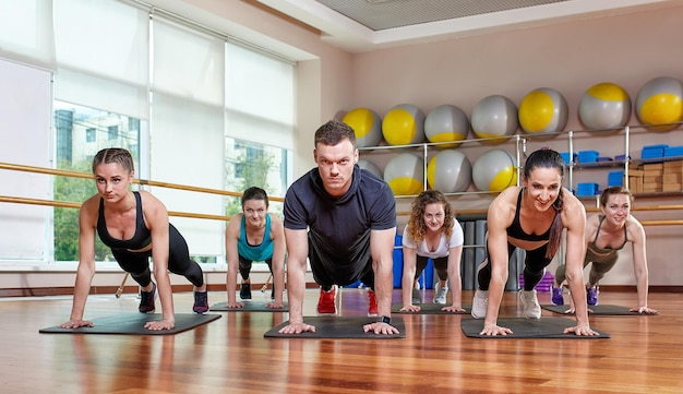 A group of sporting young people in sportswear in a fitness room doing pushups or planks in the gym Group fitness concept group workouts motivation