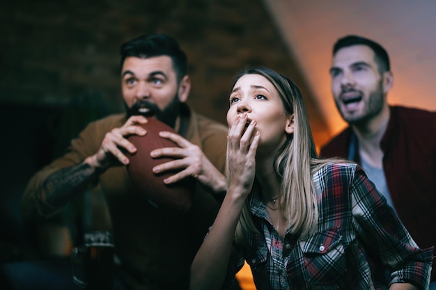 Group of sports fans feeling disappointed while watching rugby match on TV at home Focus is on shocked woman in the foreground