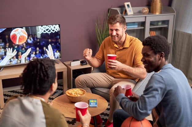 Group of sports fans watching match at home on TV and cheering