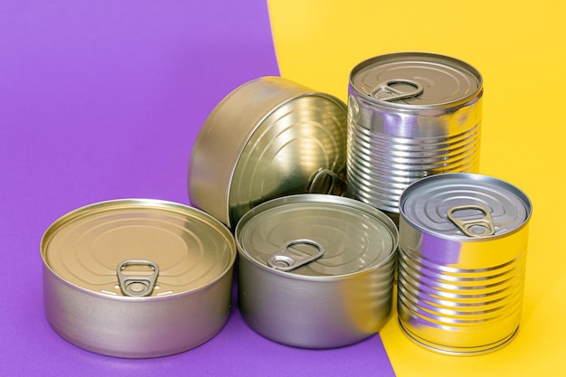 A group of stacked tin cans with blank edges on split yellow and violet background