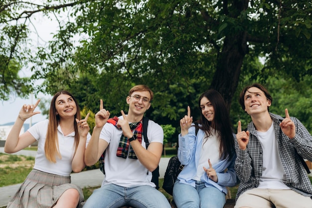 Group of student friends pointing up at copy space in park