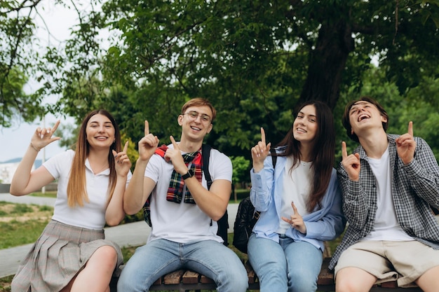 Group of student friends pointing up at copy space in park