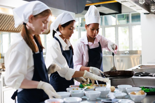 料理教室で料理教室を学んでいる学生の女の子のグループ幸せな若い女性の多民族の学生のグループは料理学校で料理教室に焦点を当てています