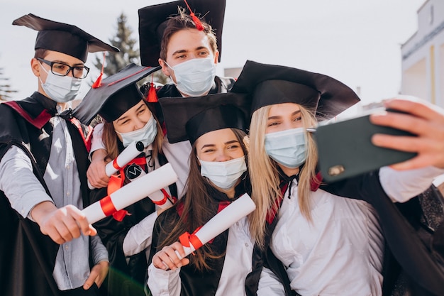 Gruppo di studenti che festeggiano insieme la laurea e indossano maschere per il viso