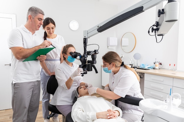 Group of students in dental clinic learn watching dental\
treatment with a microscope