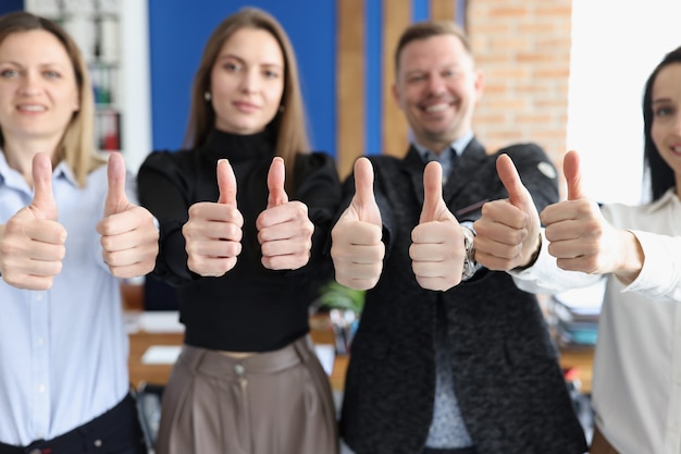 Gruppo di studenti che mostrano i pollici in su in primo piano dell'ufficio