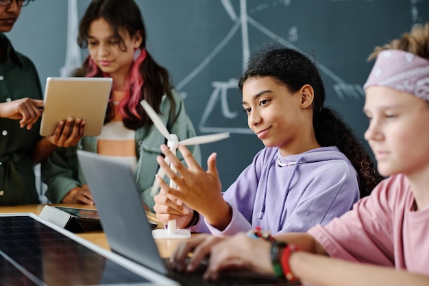 Group of students using computers and learning the work of windmill together with teacher