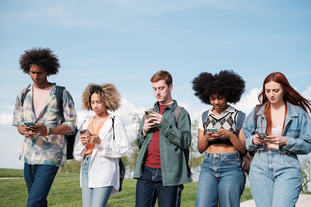 Group of students walking through the university campus looking only at the mobile Concept smartphone digital age entertainment