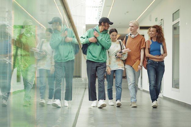 Group of stylish intercultural teenage guys and girls moving down corridor