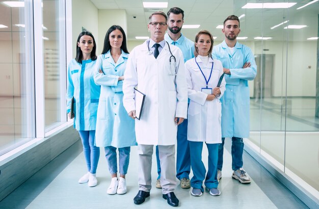 Un gruppo di medici moderni di successo e fiduciosi stanno posando e guardando la telecamera nel corridoio dell'ospedale