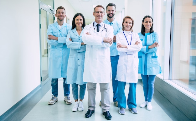 Photo group of successful and confident modern medical doctors are posing and looking on the camera at the hospital corridor