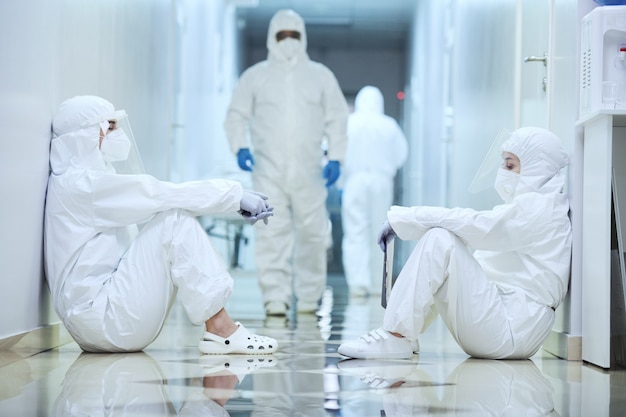 Group of surgeons in protective uniforms sitting in the corridor at hospital they working during pandemic