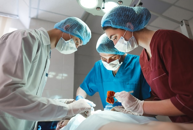 手術室で手術中の外科医のグループ。蘇生医学チームは、患者を救うスチール製の医療用具を保持する保護マスクを着用しています。手術と緊急事態。