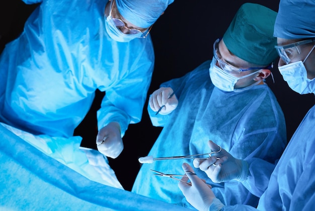 Group of surgeons at work in operating theater toned in blue Medical team performing operation